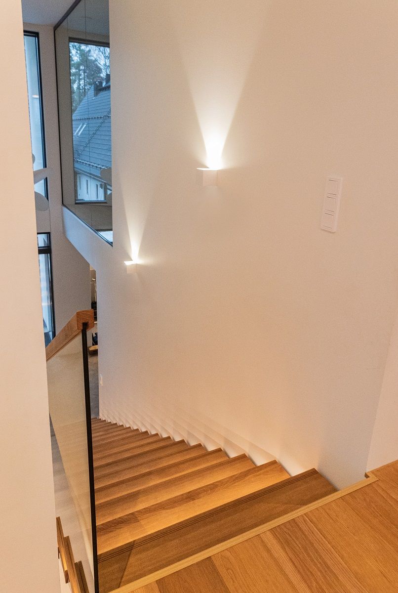 The high white wall of the staircase is illuminated by a sharp spotlight from the FUNKit wall light.